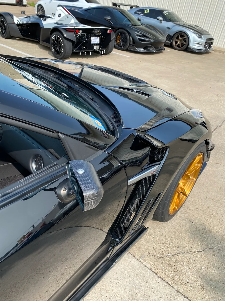 A black Nissan GT-R with gold wheels, a black McLaren, a BAC Mono, and a silver Nissan GT-R parked outdoors.