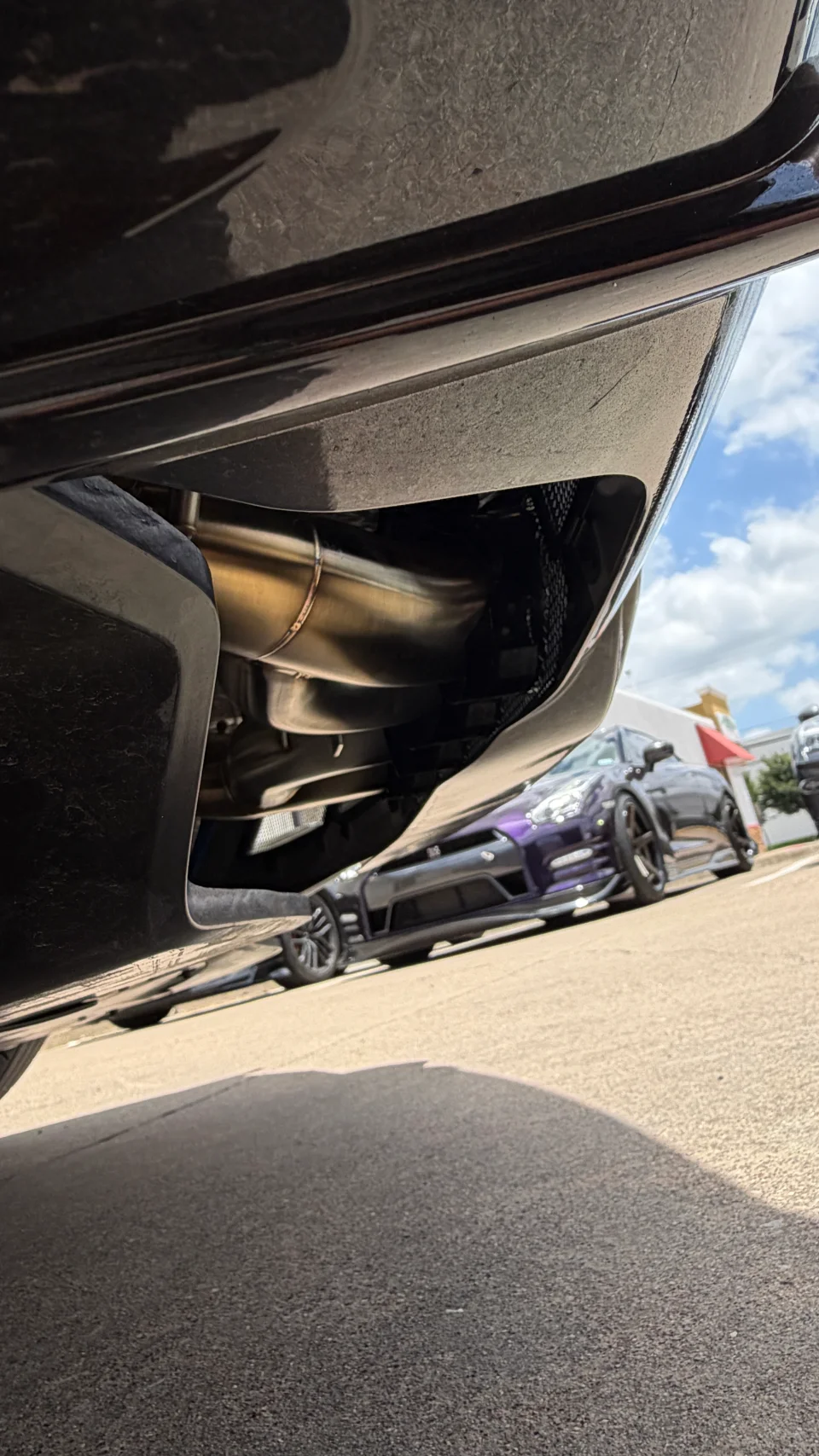 Close-up of an aftermarket exhaust system installed on a performance car, with a purple Nissan GT-R in the background.