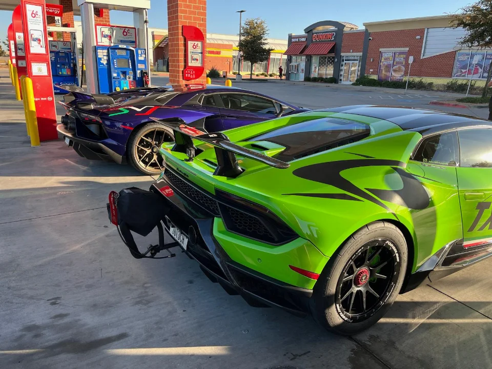 Two custom-wrapped Lamborghinis, one green and one purple, parked at a gas station with a Dunkin' in the background.