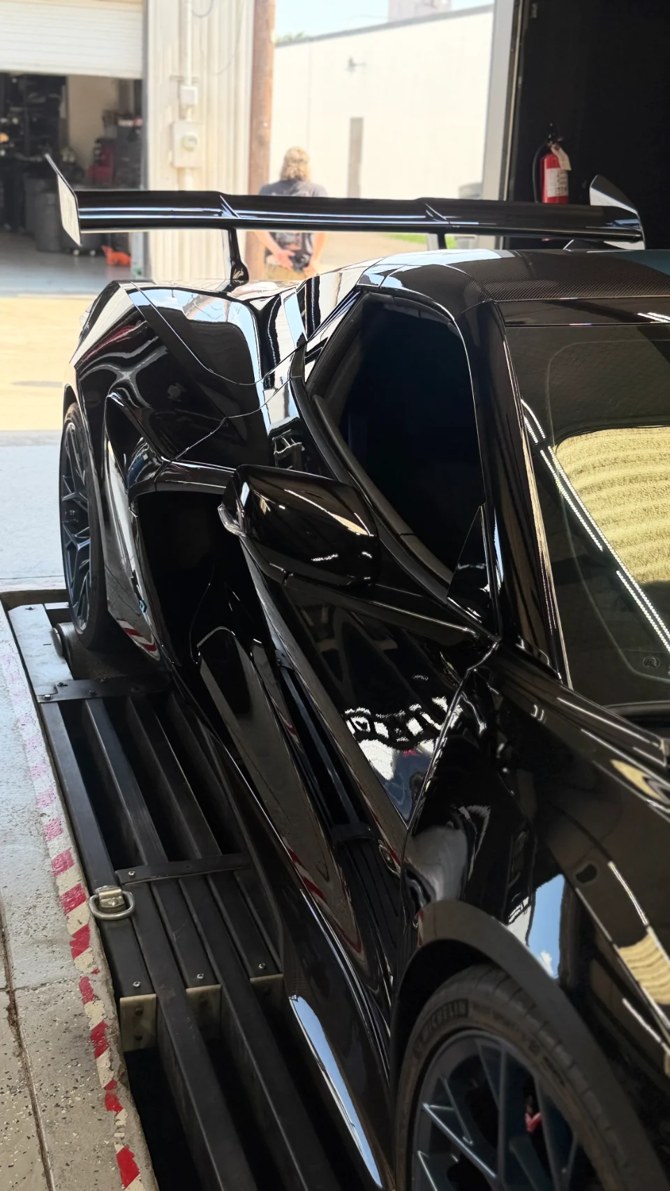 A black McLaren supercar with a large rear wing strapped to a dynamometer at a performance tuning shop.