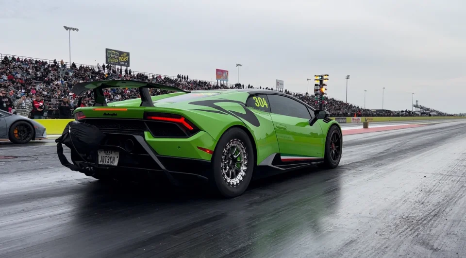A vibrant green Lamborghini Huracan race car with a large rear wing on a drag strip, poised for a race.
