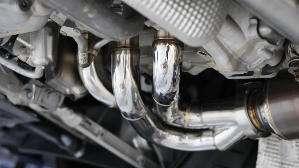 Close-up view of a performance exhaust system with polished stainless steel downpipes and muffler from underneath a car.