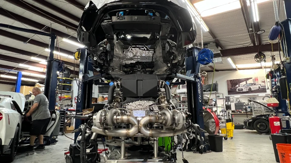A Nissan GT-R on a lift in a Jotech Motorsports shop, with its twin-turbo engine and exhaust system clearly visible.