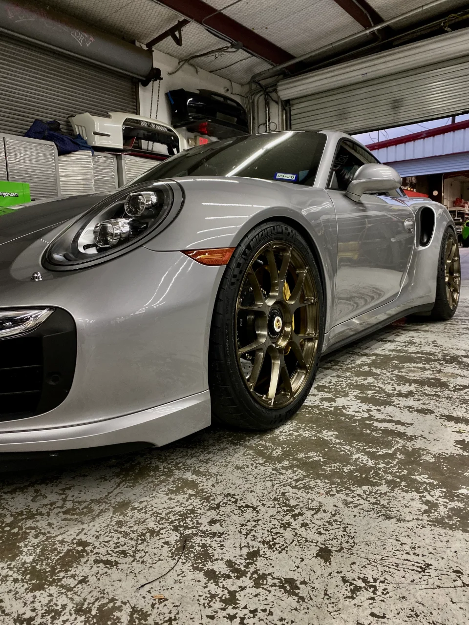 A silver Porsche 911 with bronze aftermarket wheels parked inside a performance tuning shop.