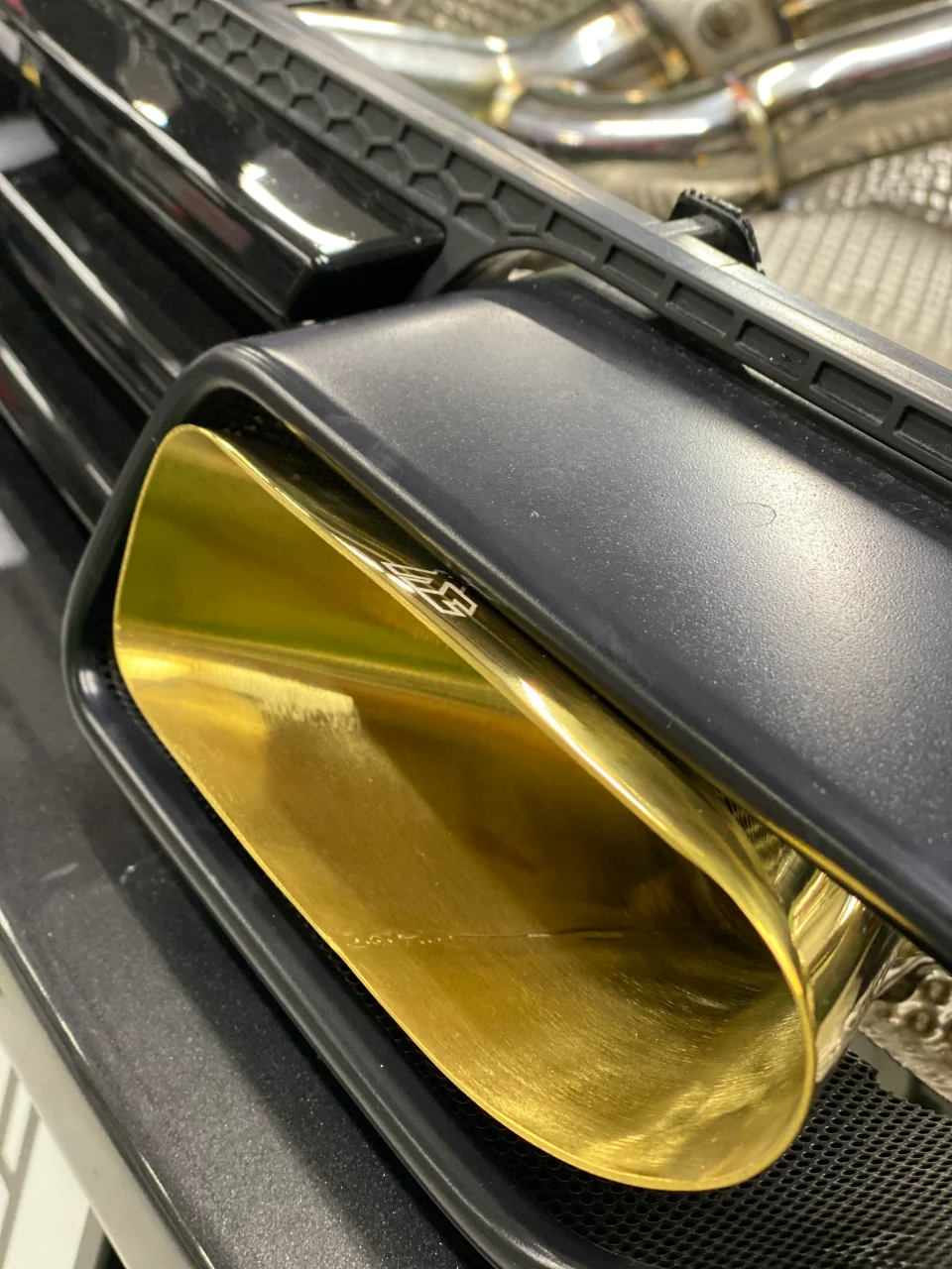 A close-up detail shot of a custom gold exhaust tip on a performance car, showcasing its unique finish.