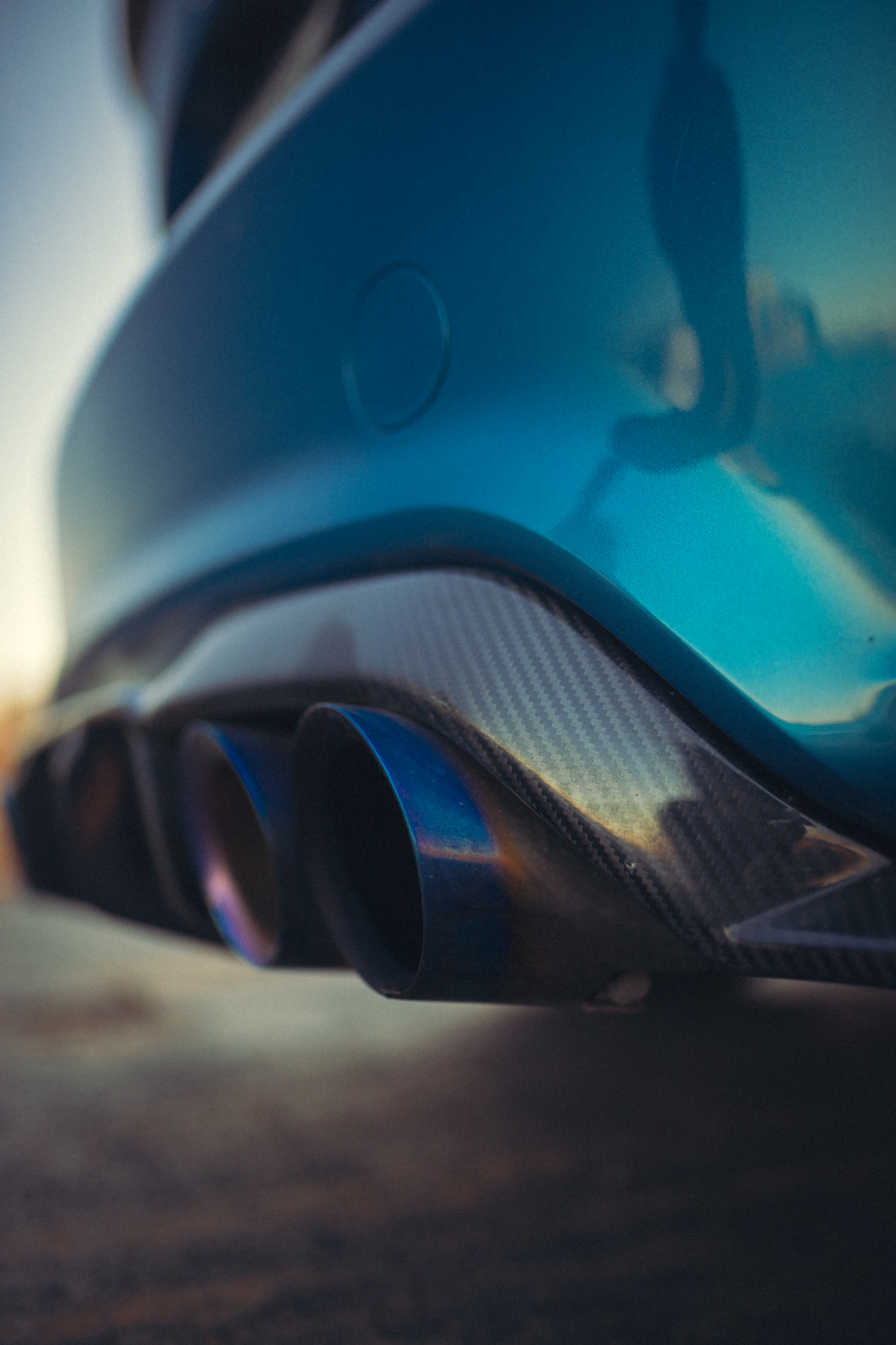 Close-up of a blue car's rear bumper featuring titanium exhaust tips and a carbon fiber diffuser.