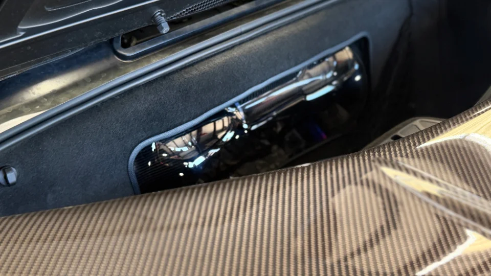 Close-up detail of a performance car's engine bay showing a carbon fiber panel and a reflective intake pipe.