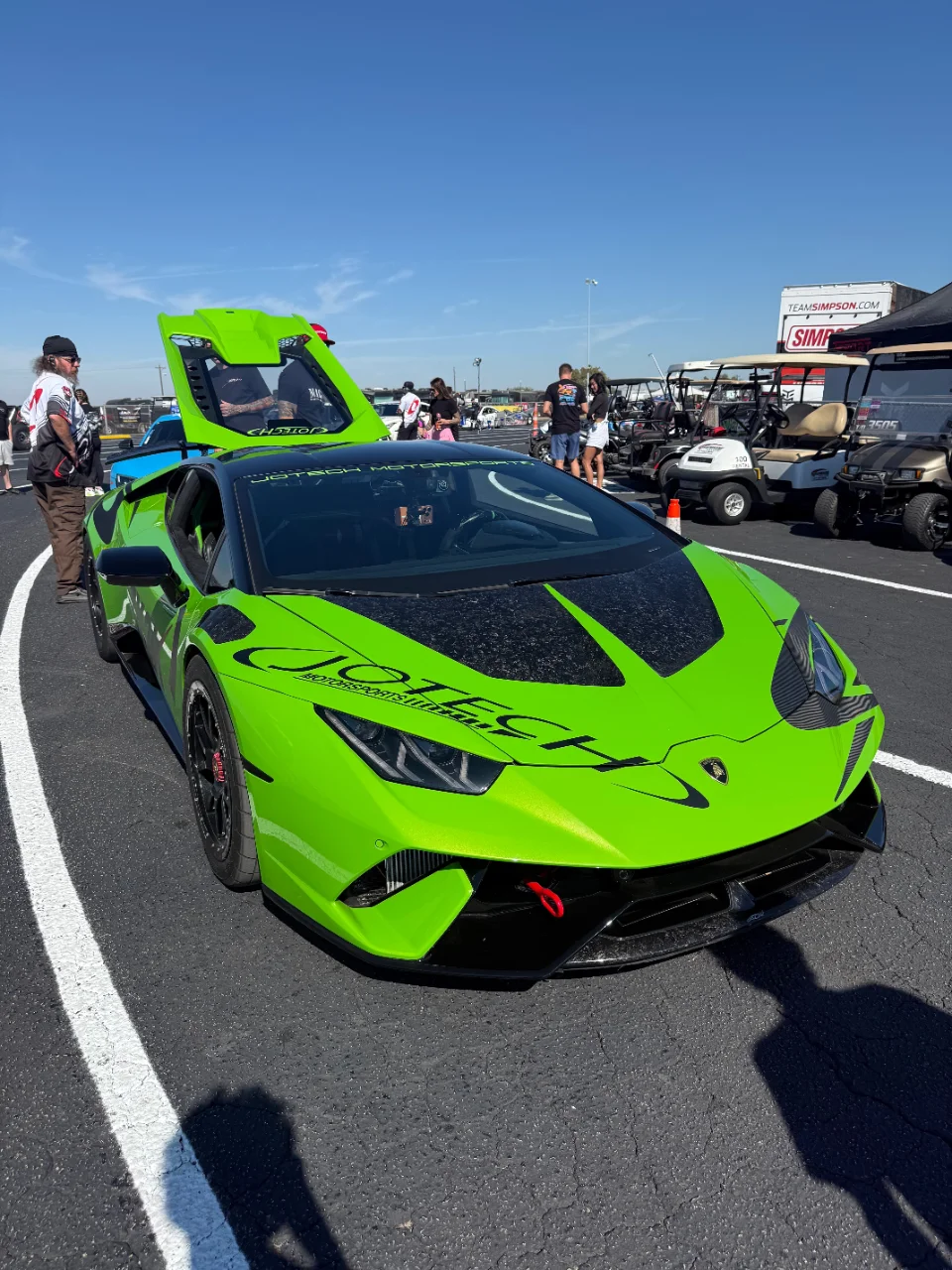 A bright green Jotech Motorsports Lamborghini Huracan with its engine cover open, parked in the pit area of a drag strip event.