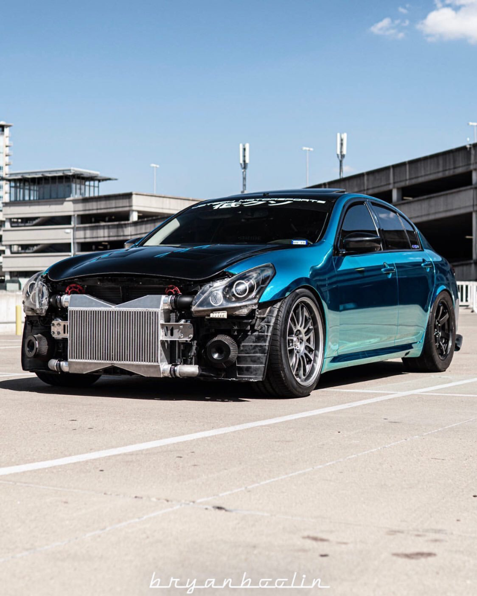 A modified blue Infiniti G37 sedan with its front bumper removed, showcasing a large intercooler and turbo setup, parked in an outdoor lot.