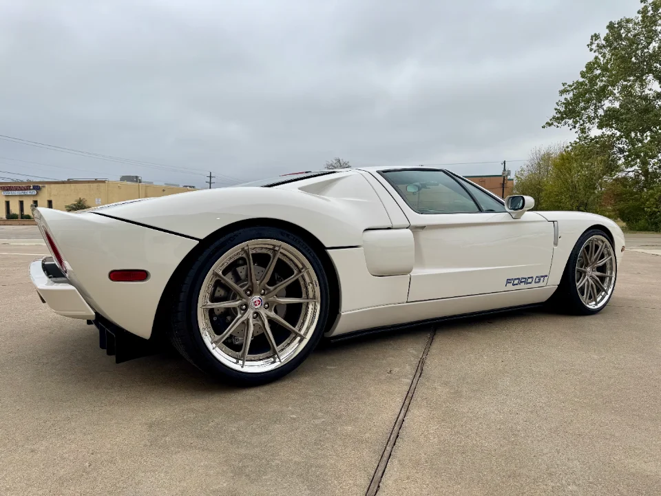 White Ford GT with aftermarket HRE wheels and a rear diffuser parked on concrete under a cloudy sky.