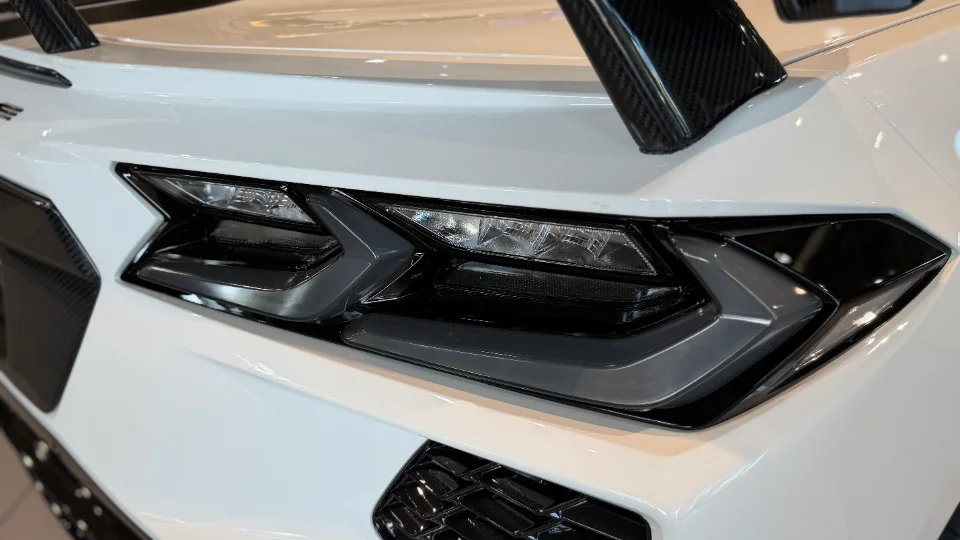 A close-up detail of a white Corvette's rear LED headlight and carbon fiber wing, showcasing modern automotive design.
