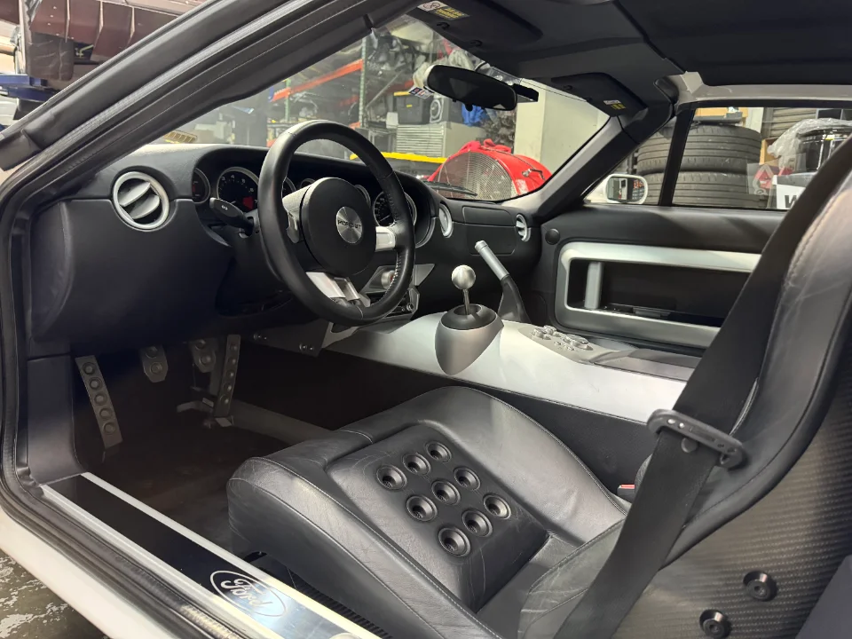 Interior view of a Ford GT cockpit showing the steering wheel, manual shifter, sport seat, and pedals.