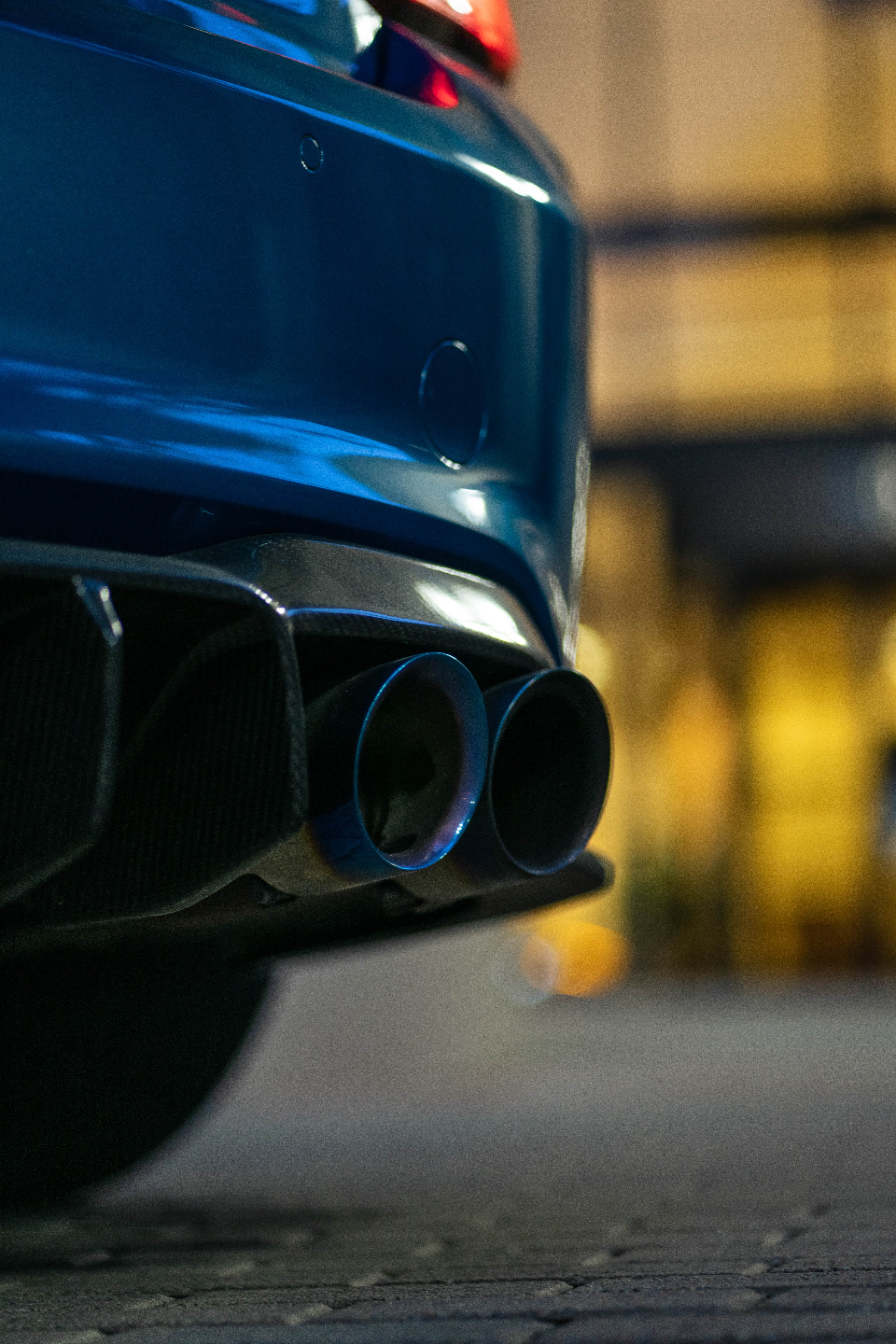Close-up of the rear of a blue car, showcasing aftermarket exhaust tips with a carbon fiber diffuser.