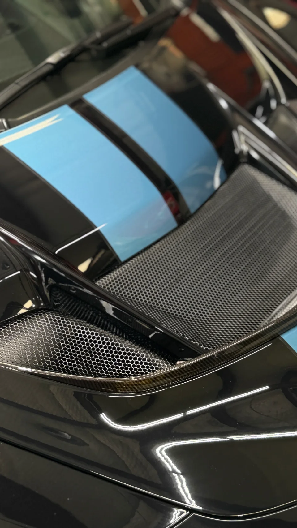 Close-up detail of a black McLaren's engine cover with blue racing stripes and carbon fiber grilles.