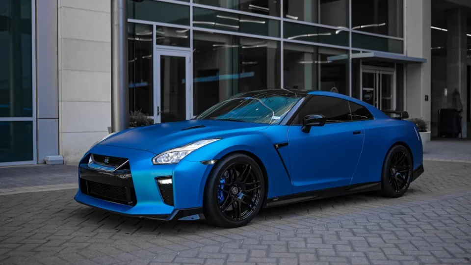 Matte blue Nissan GT-R with black multi-spoke wheels parked in front of a modern glass building.