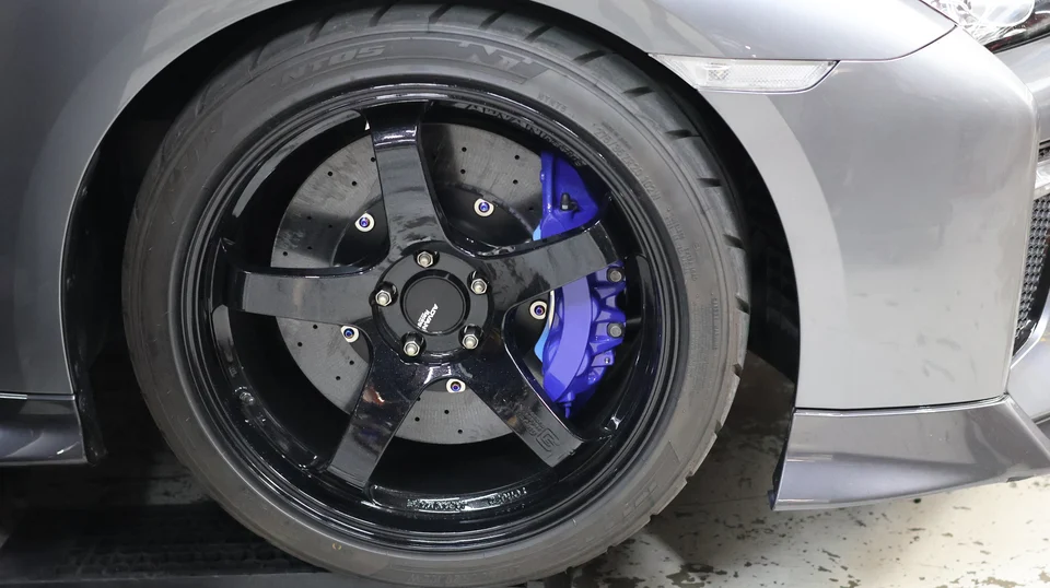 A close-up of a gray Nissan GT-R's black Advan Racing wheel, Nitto tire, and blue brake caliper.