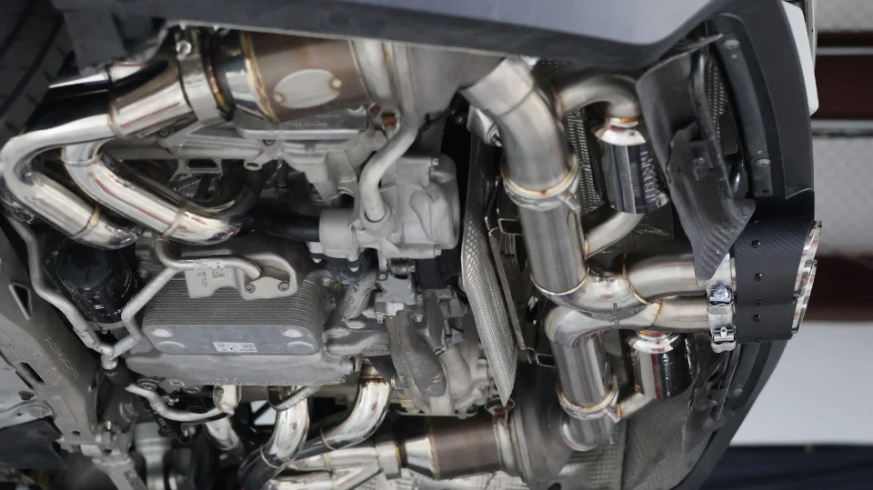Underside view of a performance car showcasing a custom stainless steel exhaust system and other drivetrain components.