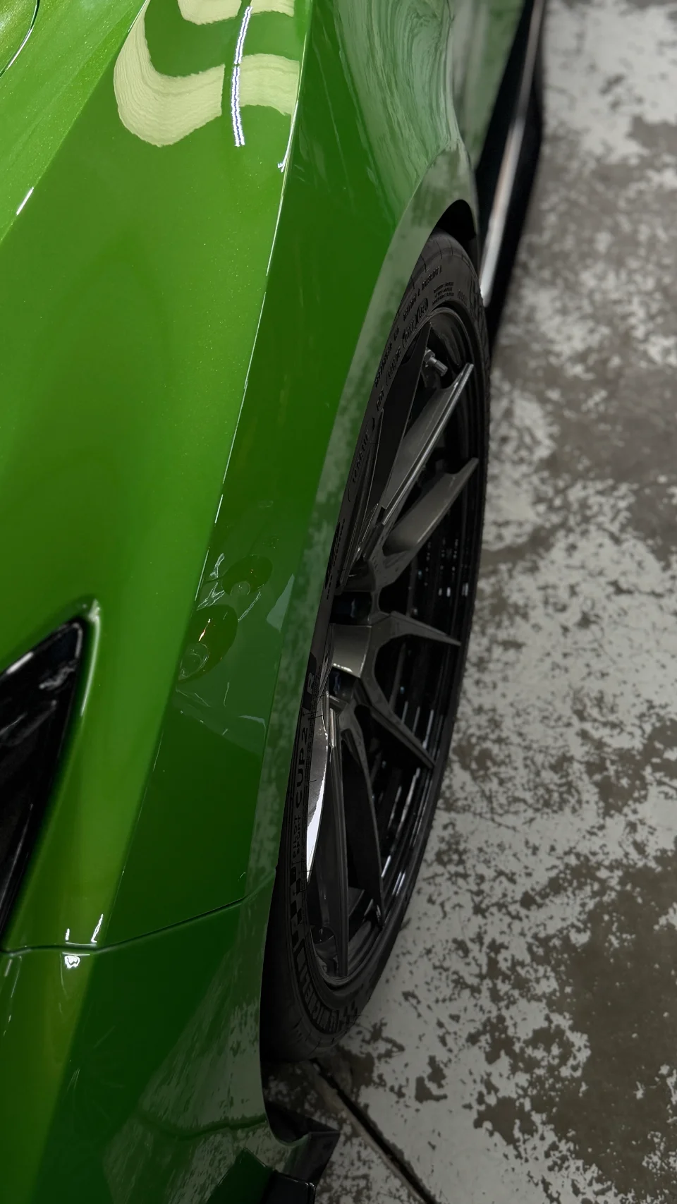 Close-up of a vibrant green car's fender and custom black multi-spoke wheel with Michelin tires.