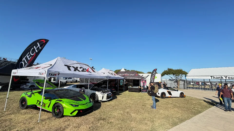 A green Lamborghini Huracan and a white Nissan GT-R displayed under Jotech and TX2K tents at an outdoor car show.