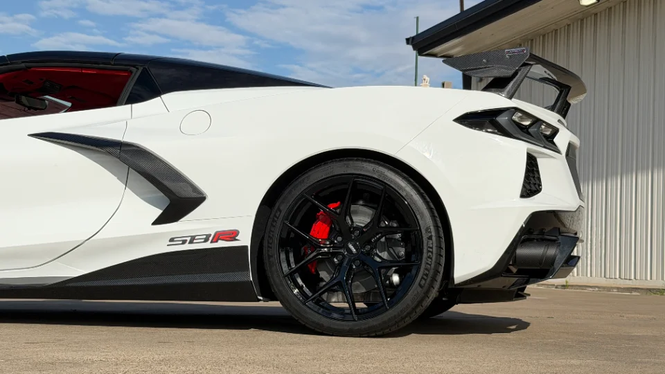 A white Corvette C8 with black aftermarket wheels, red brake calipers, and carbon fiber aerodynamic parts including a large rear wing.