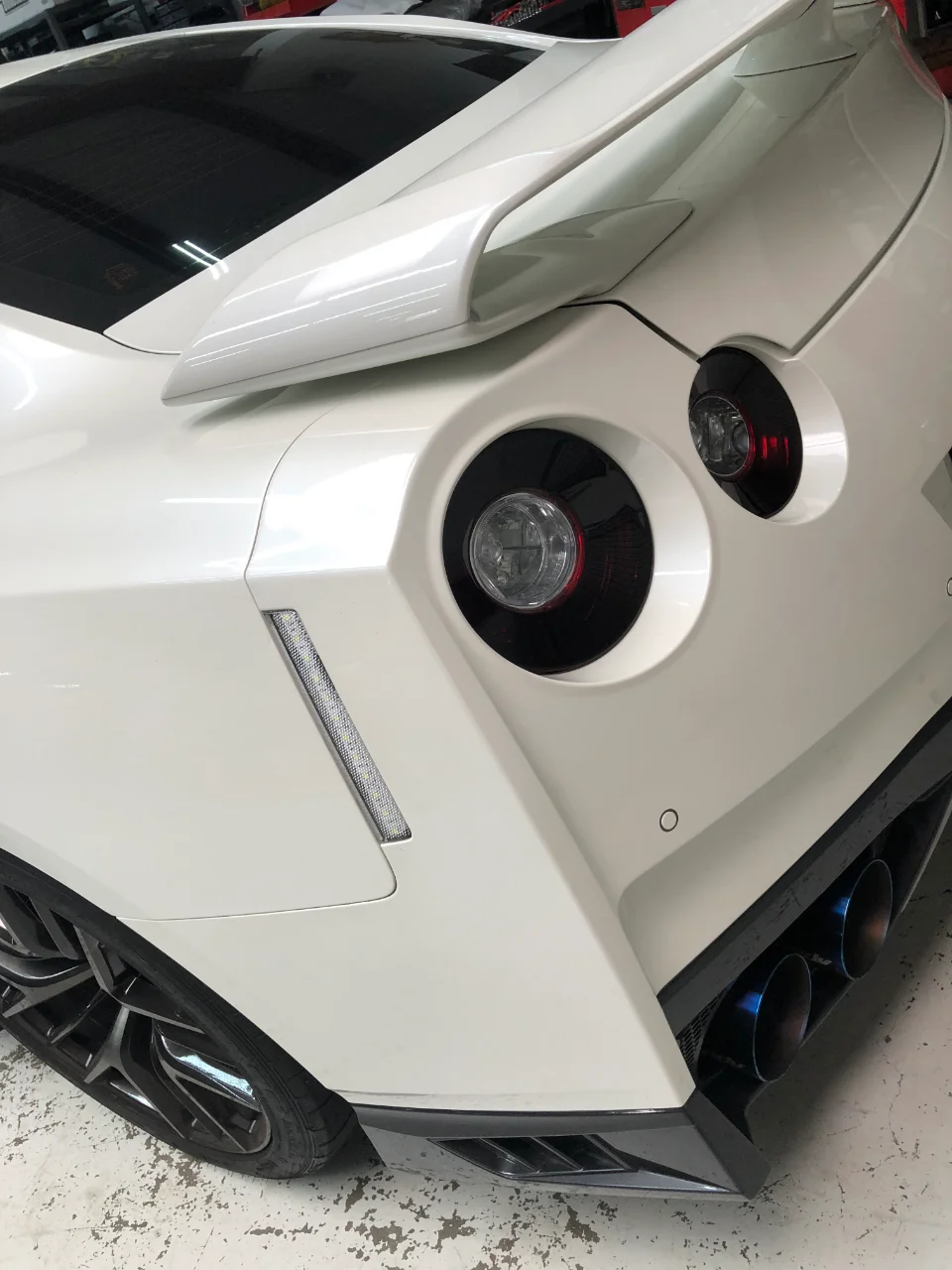Rear view of a white Nissan GT-R showcasing its large rear spoiler, diffuser, and blue-tipped aftermarket exhaust.