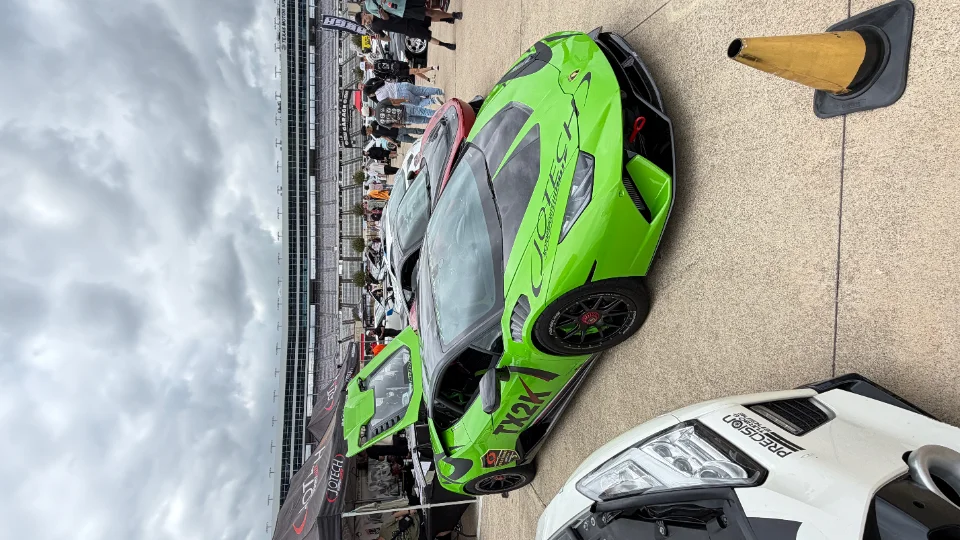 A vibrant green Lamborghini Huracan race car with Jotech livery parked at a track event, with a grandstand and spectators in the background.