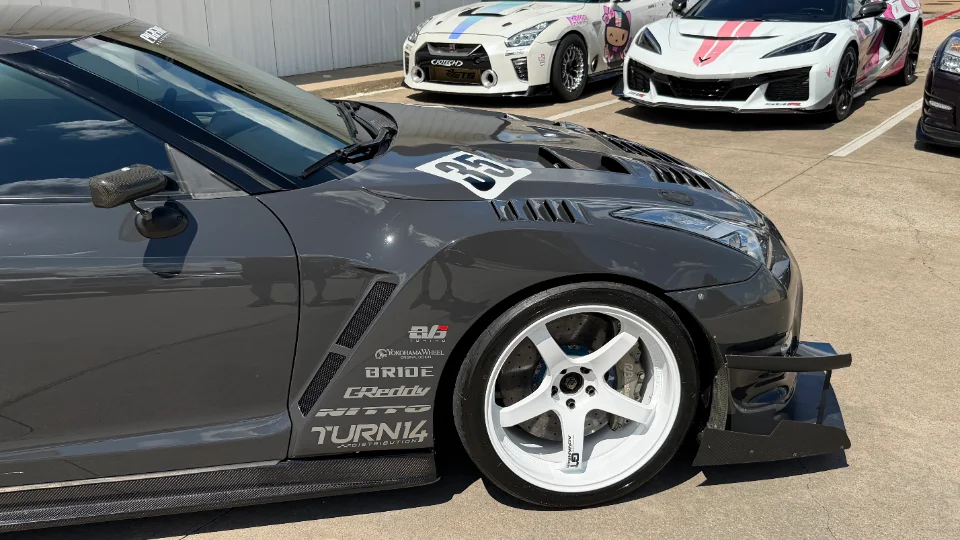 A grey Nissan GT-R with a widebody kit, carbon fiber aero, and white aftermarket wheels parked outdoors.