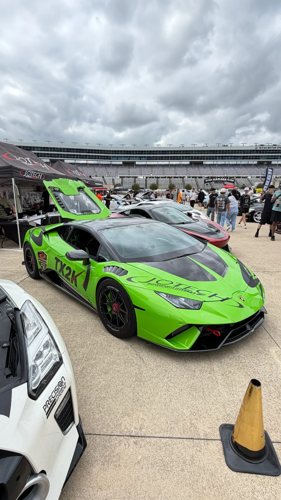 A vibrant green Lamborghini Huracan race car with Jotech livery parked at a track event, with a grandstand and spectators in the background.