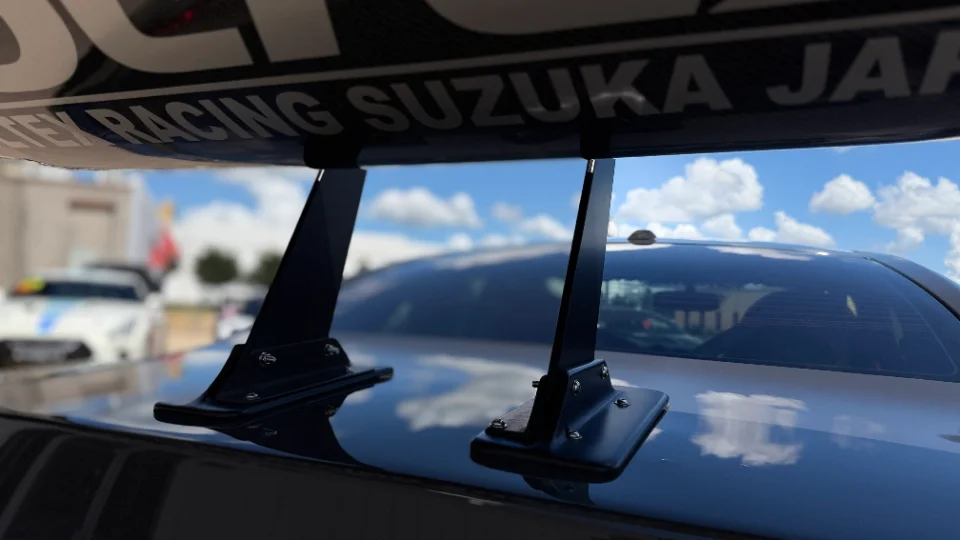 Close-up of a performance car's large rear wing with 'RACING SUZUKA JAPAN' visible on the underside, at an outdoor event.