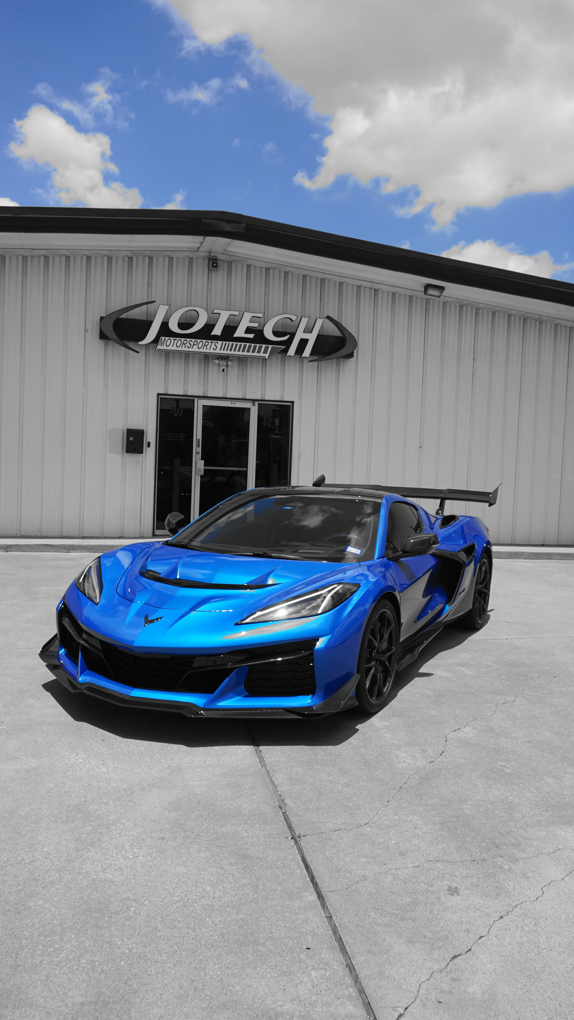 Blue Chevrolet Corvette C8 Z06 with a large rear wing parked in front of the Jotech Motorsports shop.