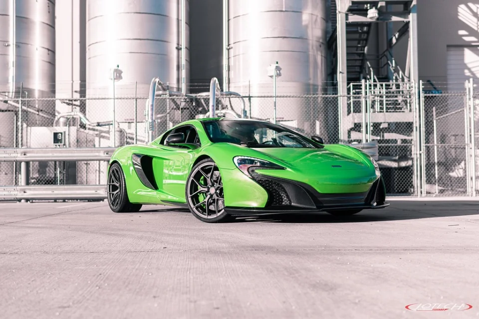 A vibrant green McLaren supercar with custom wheels and carbon fiber accents parked in an industrial setting.