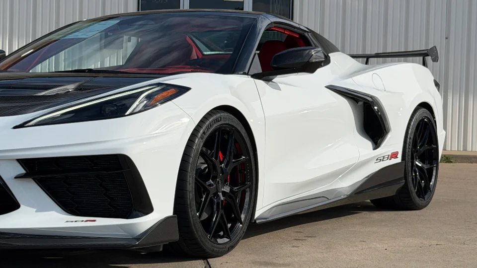 A white Corvette C8.R with carbon fiber aero, black wheels, and red brake calipers parked outdoors.