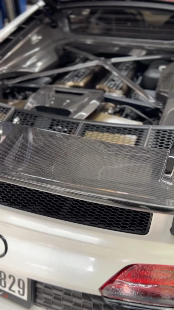 Close-up of a white Audi R8 engine bay with a V10 engine, carbon fiber engine cover, and strut bar.