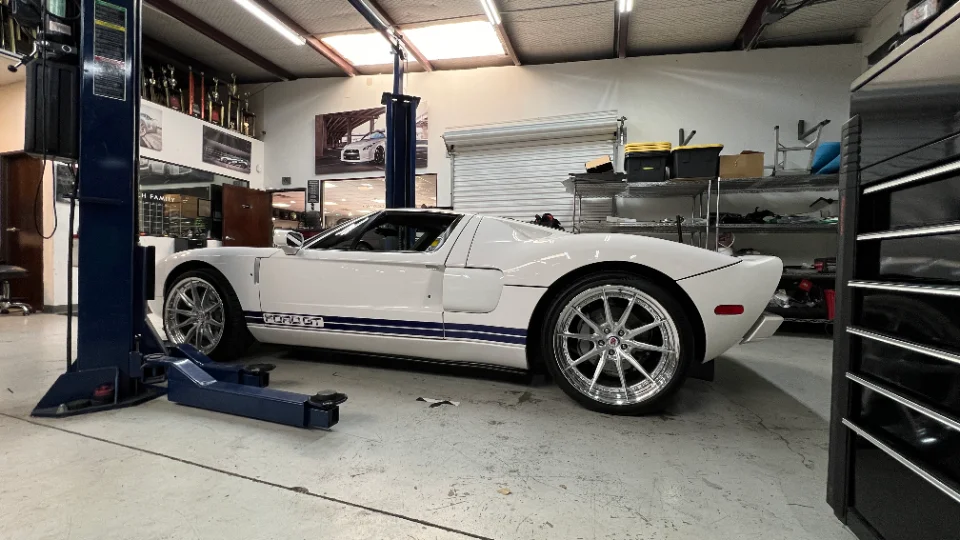 A white Ford GT with blue racing stripes and custom wheels parked in a professional automotive shop with a car lift.