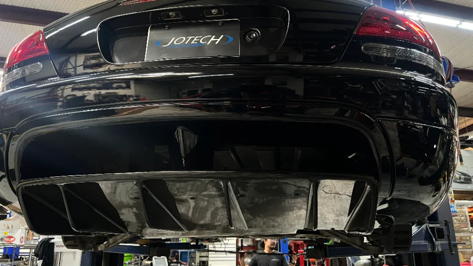 Black car on a lift in a Jotech shop, showcasing a carbon fiber rear diffuser and bumper.