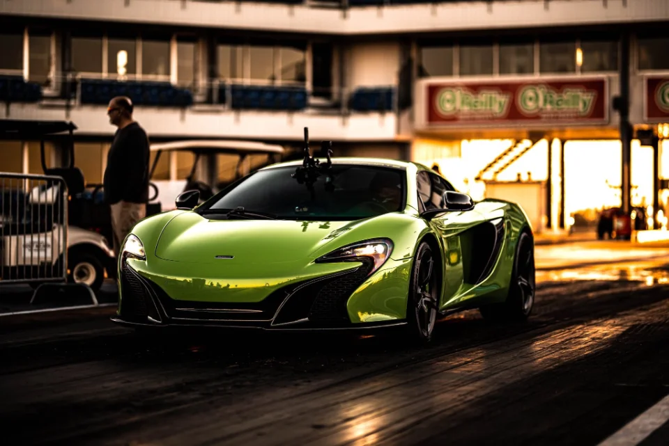 A vibrant green McLaren supercar sits on a drag strip at sunset, with a person and golf cart in the background.