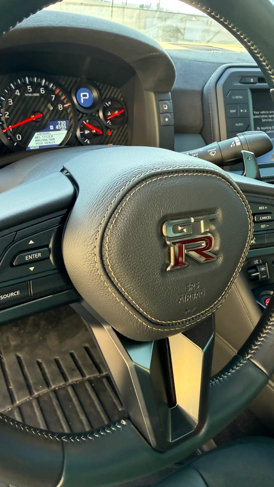 Close-up of a Nissan GT-R interior, showing the leather steering wheel with GT-R logo and carbon fiber dashboard.