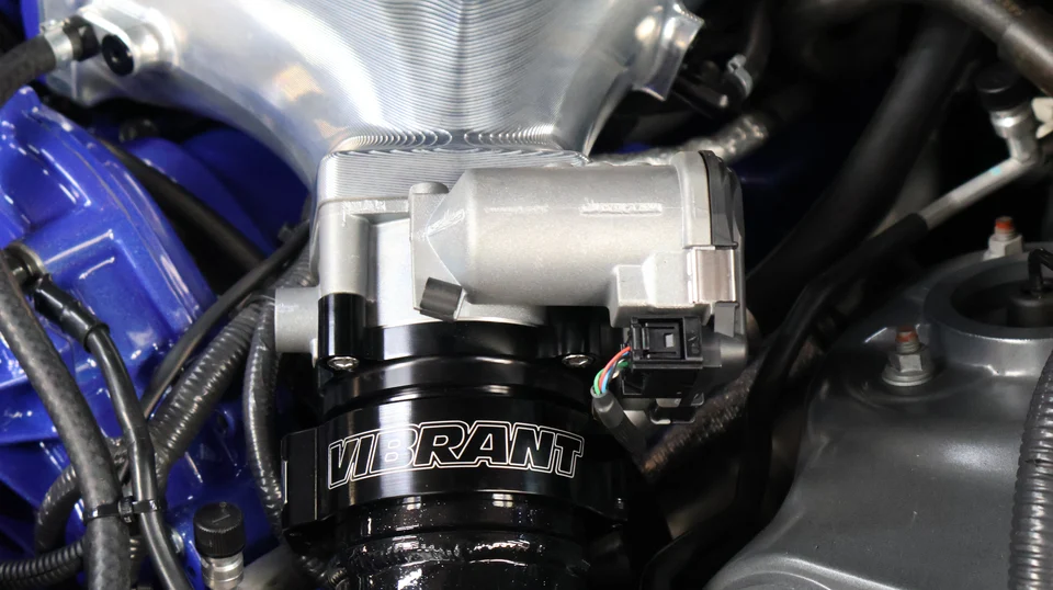 A close-up detail of a custom aluminum intake manifold and Vibrant Performance throttle body in a performance car's engine bay.