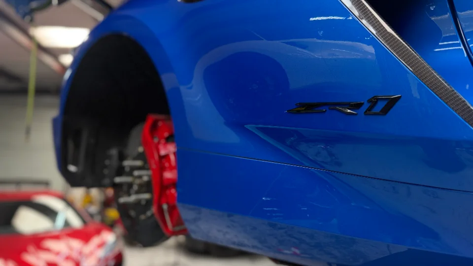 A blue Corvette Z06 on a lift in a shop, with its wheel removed, showcasing red brake calipers and the Z06 badge.
