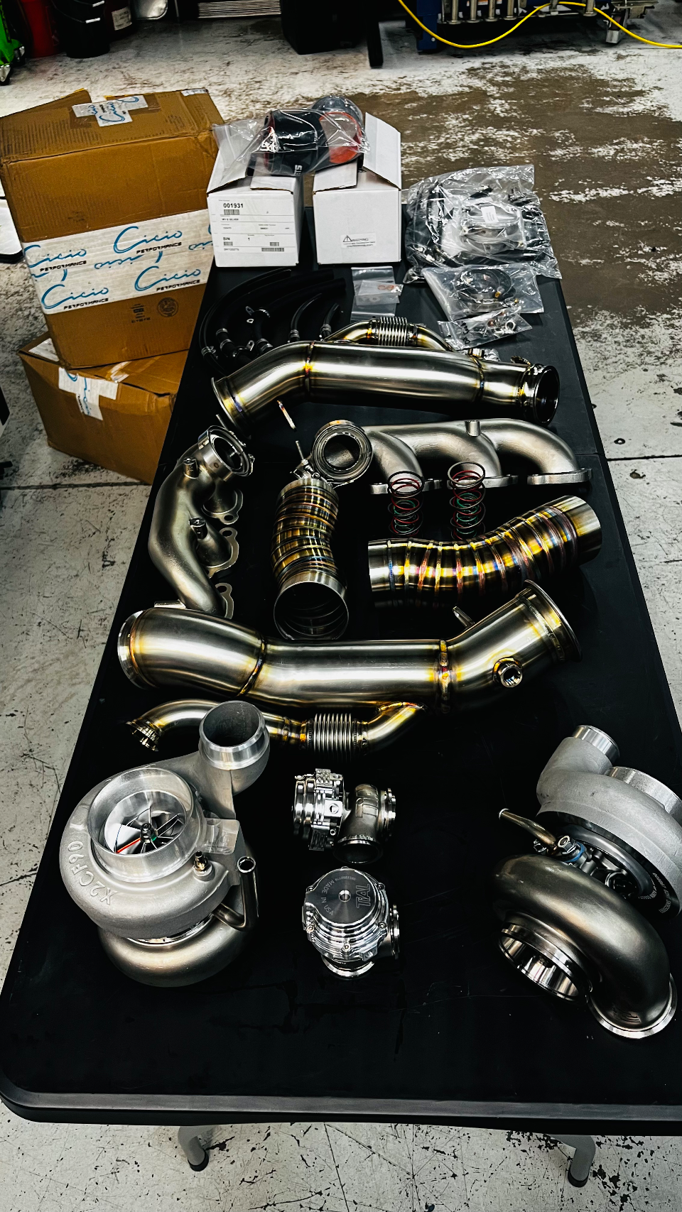High-performance turbochargers, wastegates, and stainless steel exhaust components laid out on a table in a tuning shop.