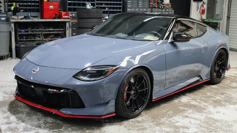 A grey Nissan Z Nismo sports car with black aftermarket wheels and red accents parked in a performance shop.