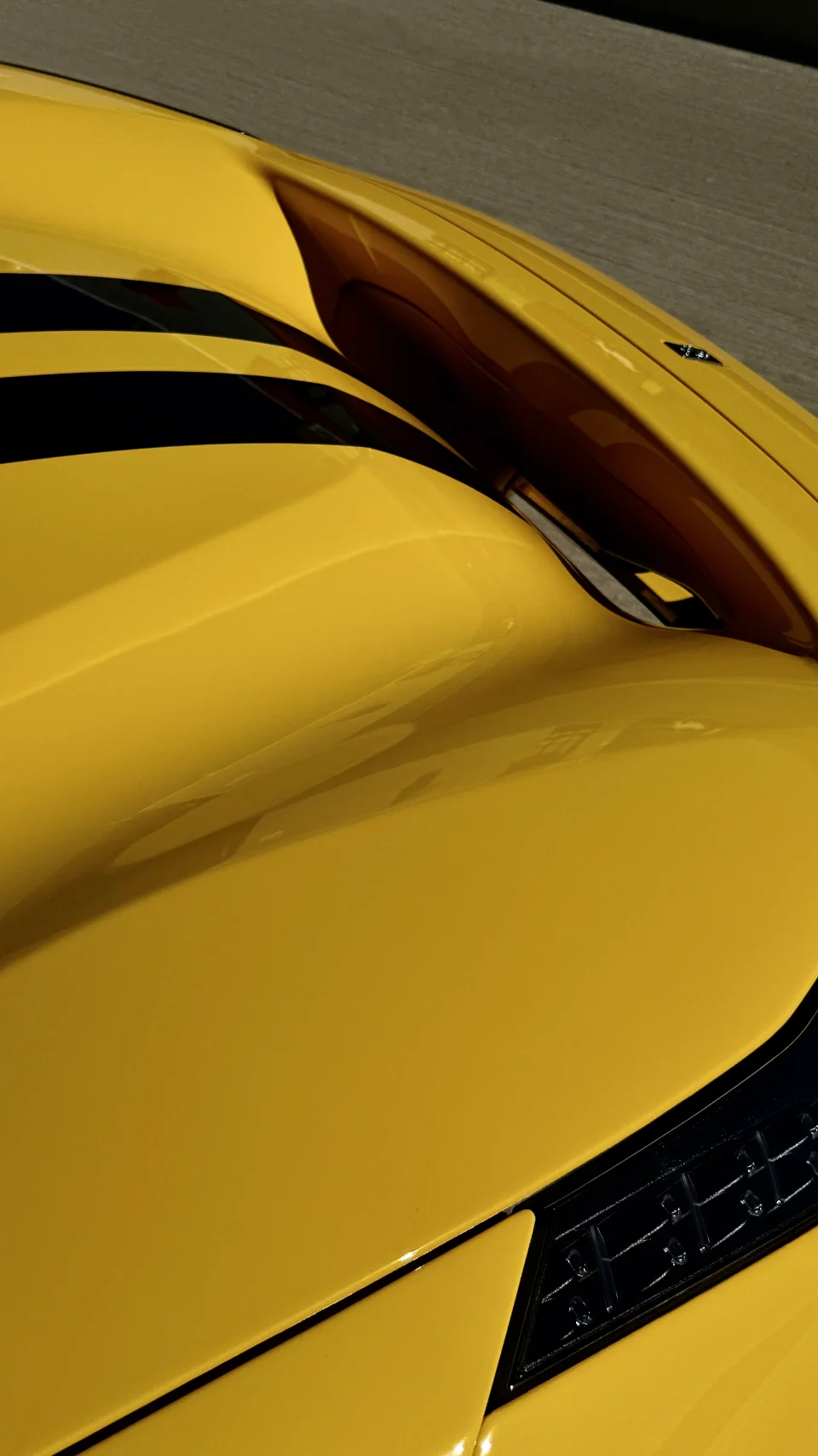 Close-up detail of a yellow supercar's hood with black racing stripes and vents, showcasing the sleek design.