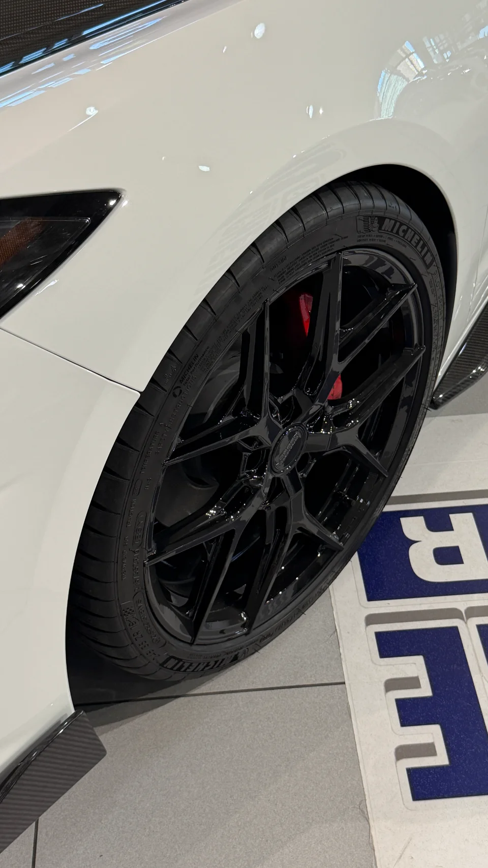 A close-up of a white car's front wheel, featuring black Vossen wheels, Michelin tires, and red brake calipers.
