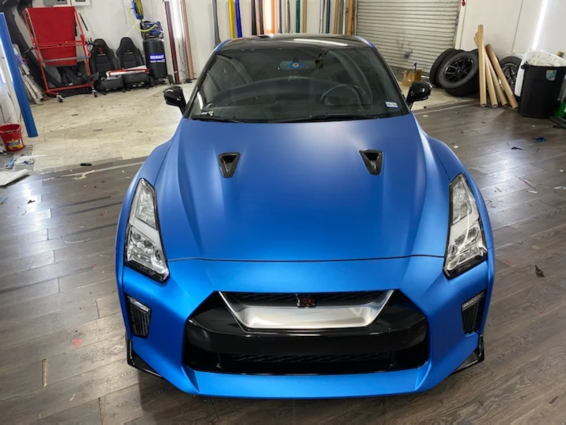 Front view of a Nissan GT-R with a matte blue vinyl wrap in a car customization shop.