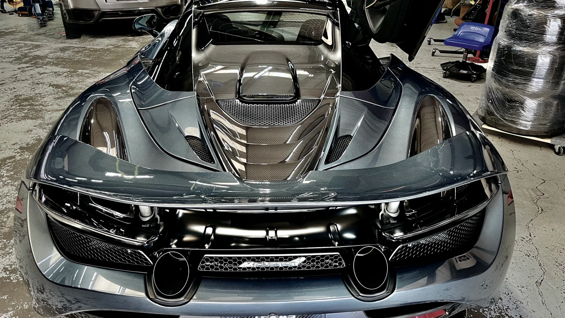 Rear view of a grey McLaren supercar with carbon fiber engine cover and diffuser in a performance tuning shop.