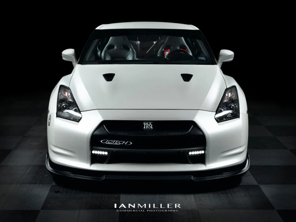 A front view of a white Nissan GT-R with Jotech branding, professionally photographed in a studio setting with a dark background.