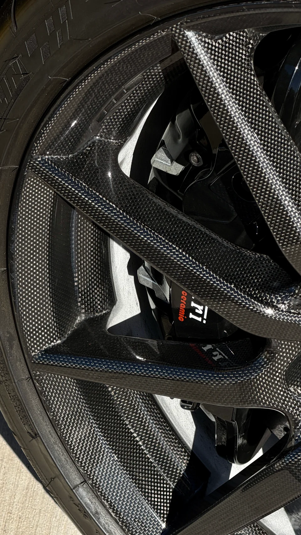 A close-up detail shot of a carbon fiber wheel and a red Porsche Carbon Ceramic Brake caliper on a performance car.