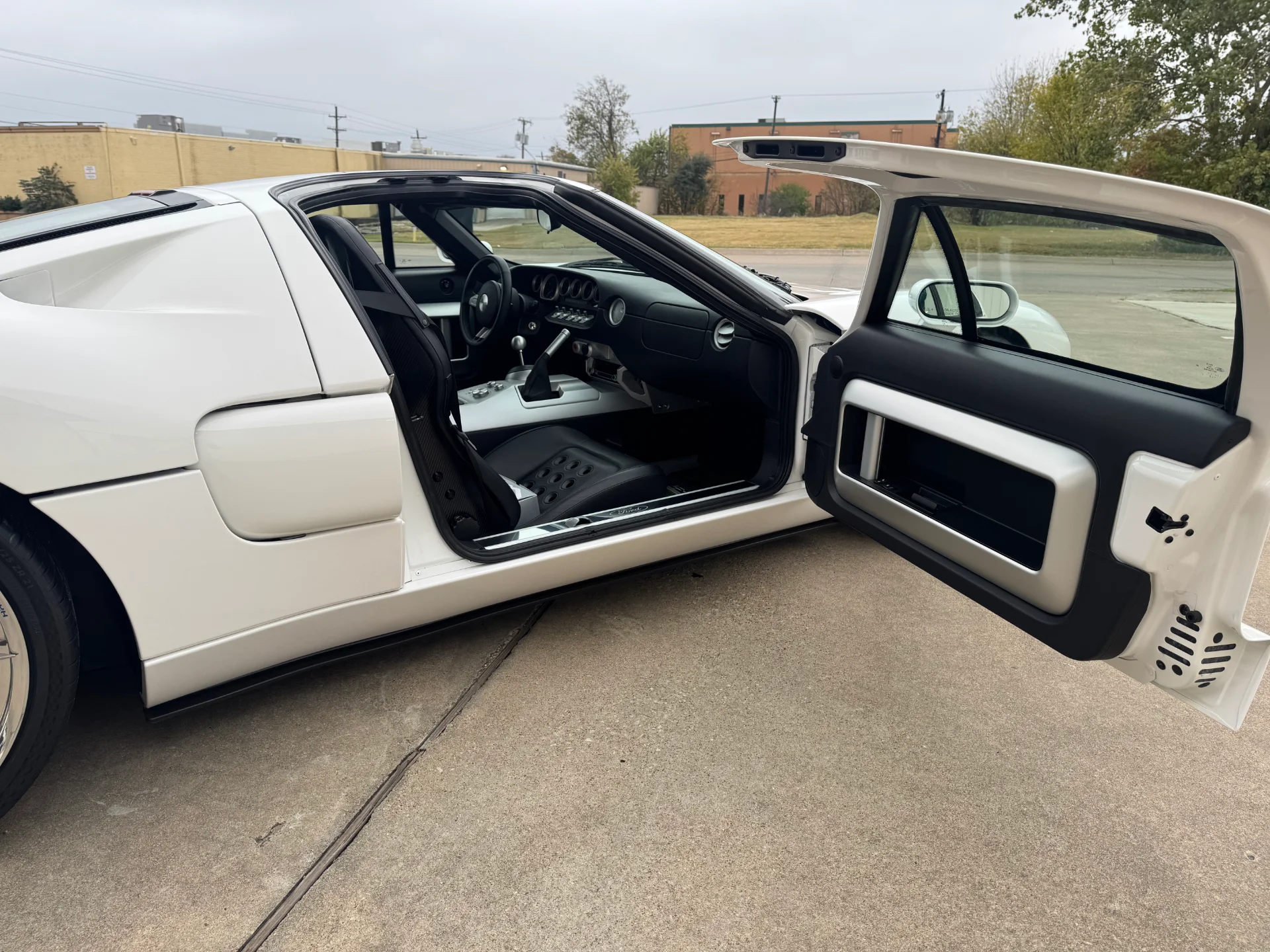 White Ford GT supercar parked outdoors with the driver's side door open, revealing the black and silver interior.