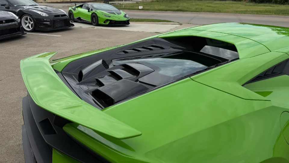A vibrant green Lamborghini Huracan parked with its rear wing visible, alongside a black Nissan GT-R in the background.