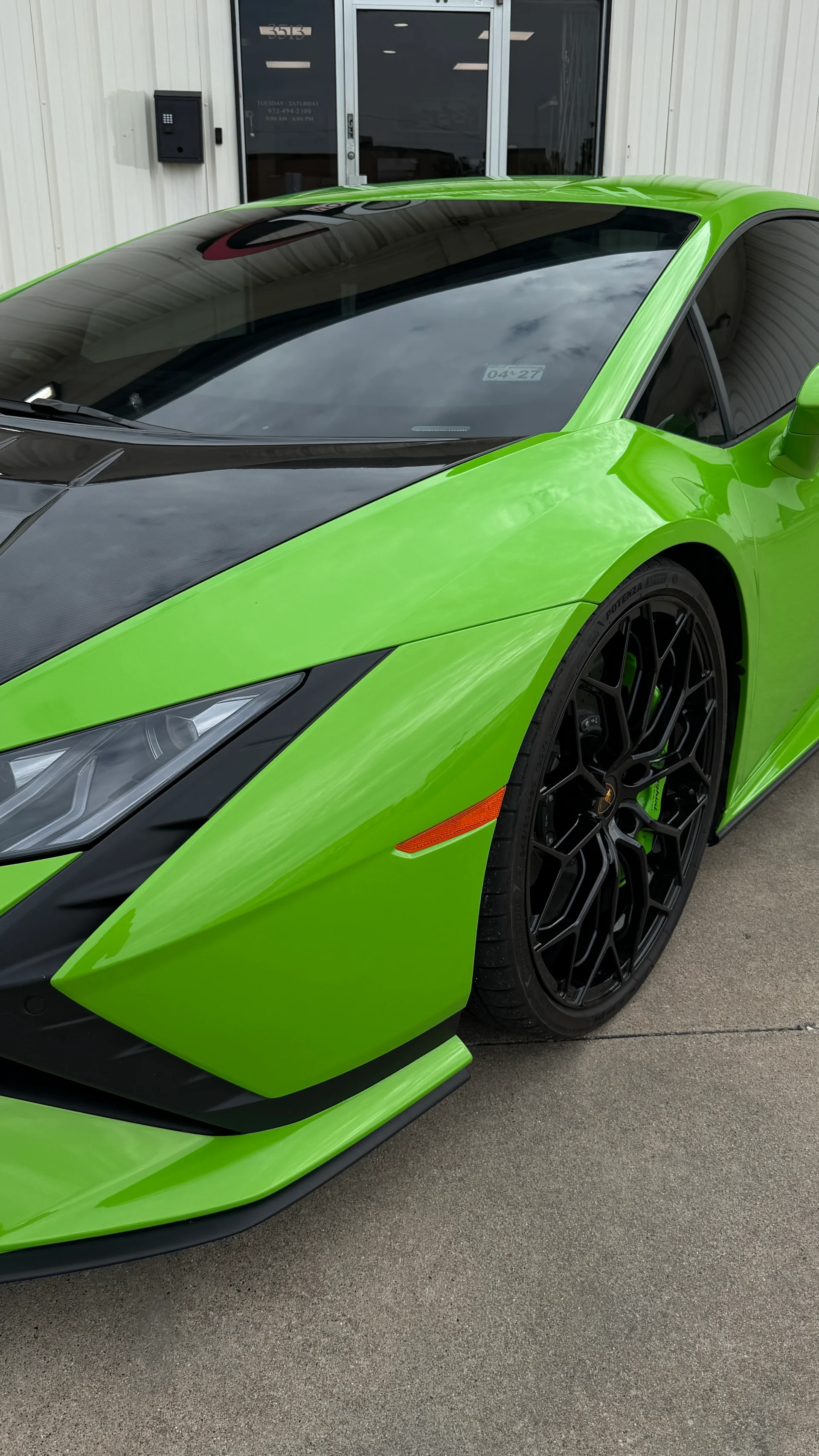A bright green Lamborghini Huracan with black wheels and a carbon fiber hood parked outside a building.